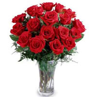 18 Roses artfully arranged in a glass vase with greens